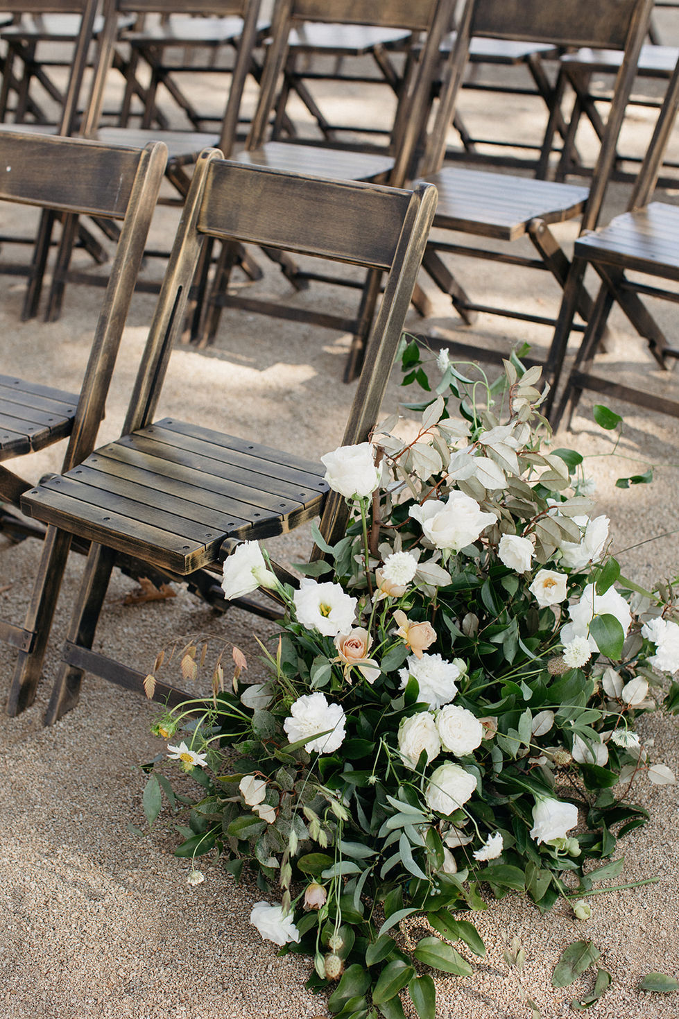 a row of wooden folding chairs with white flowers in front of them