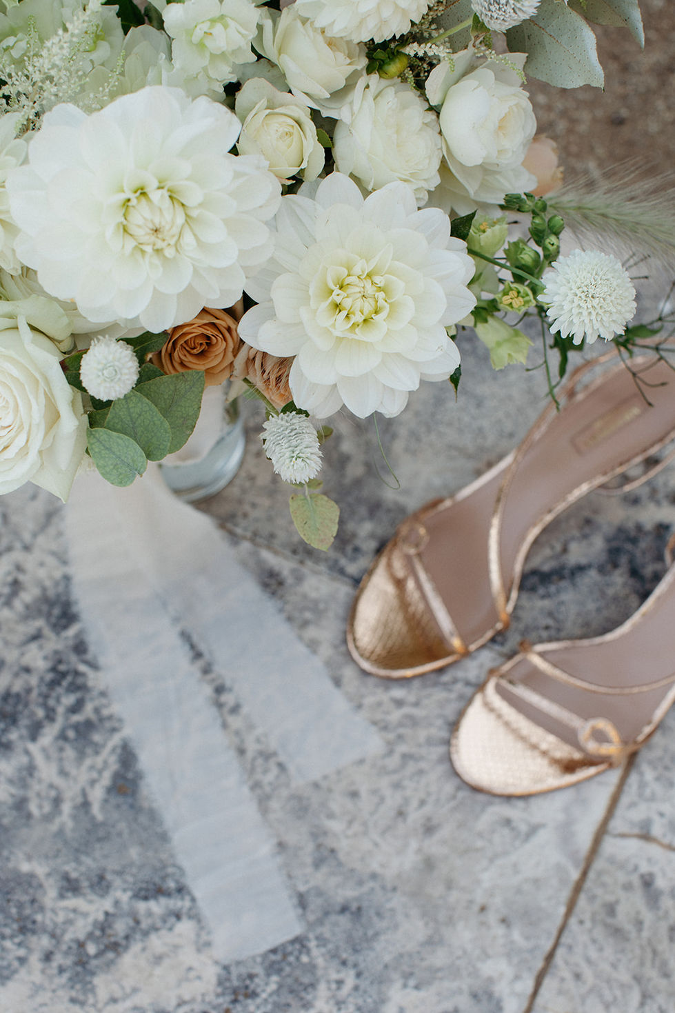 a pair of gold shoes sit next to a vase of white flowers