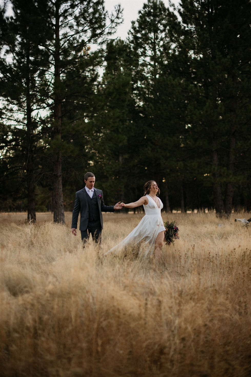 a bride and groom are walking through a field holding hands