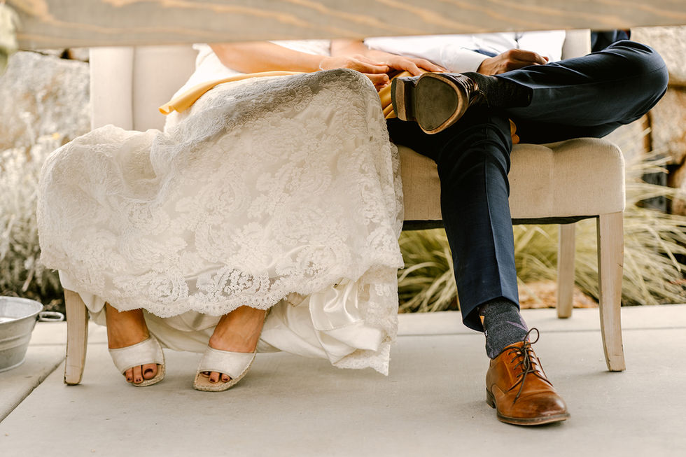 a bride and groom sit on a bench with their legs crossed