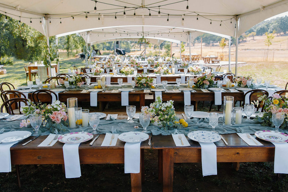a long table with plates and glasses on it under a tent