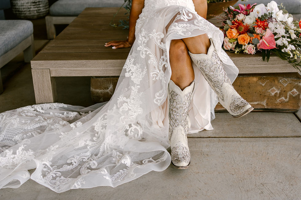 a woman in a wedding dress and cowboy boots sits on a bench