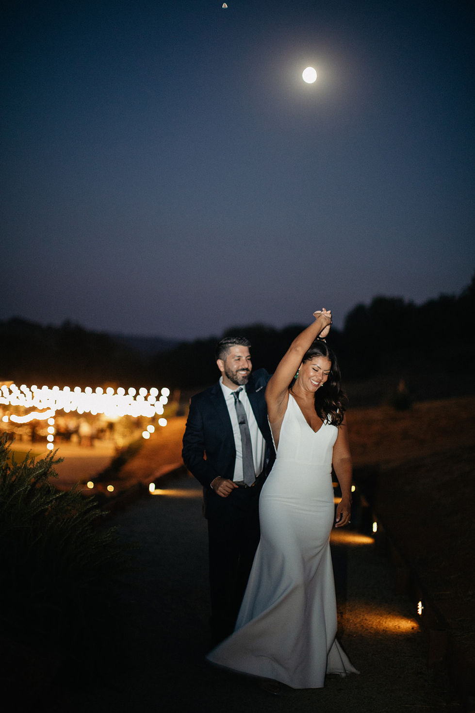 a bride and groom are dancing in front of a string of lights
