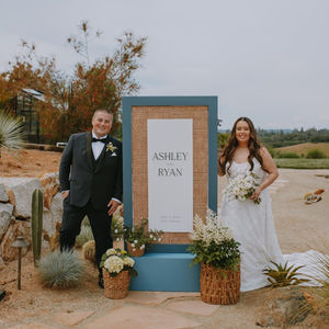 a bride and groom stand in front of a sign that says ashley and ryan