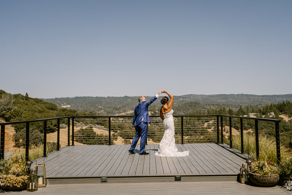 a bride and groom are dancing on a deck overlooking mountains