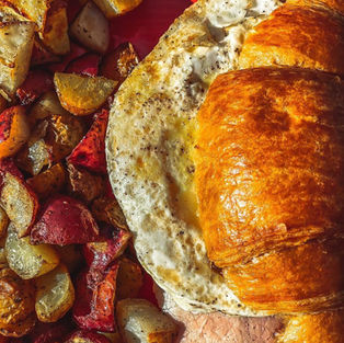 croissant breakfast sandwich with ham and eggs with a side of potatoes