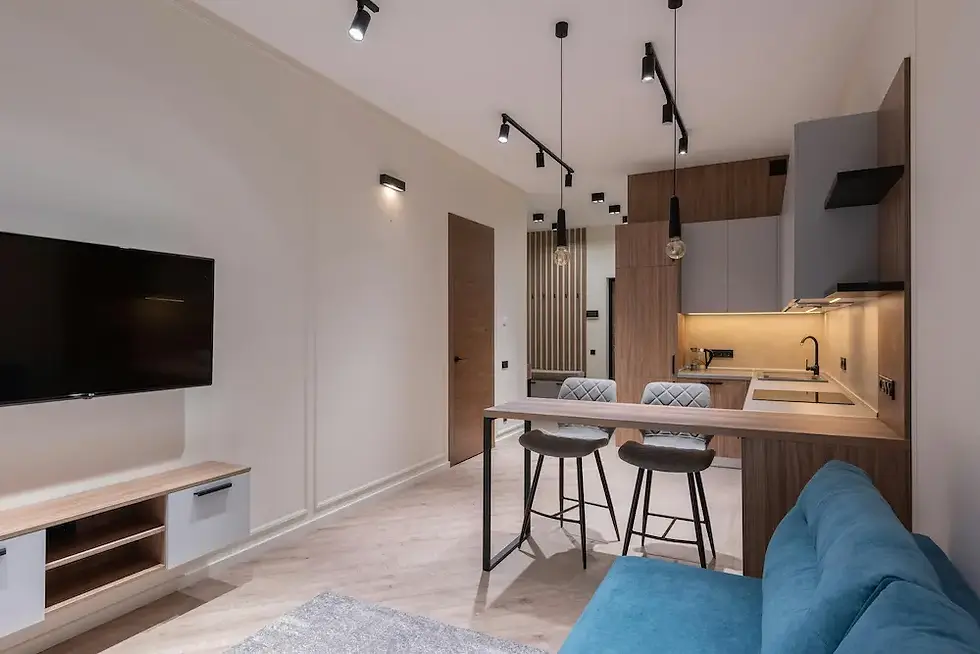 Layered lighting in studio apartment track lighting, pendant lights over kitchen bar, and under-cabinet warm glow creating distinct zones