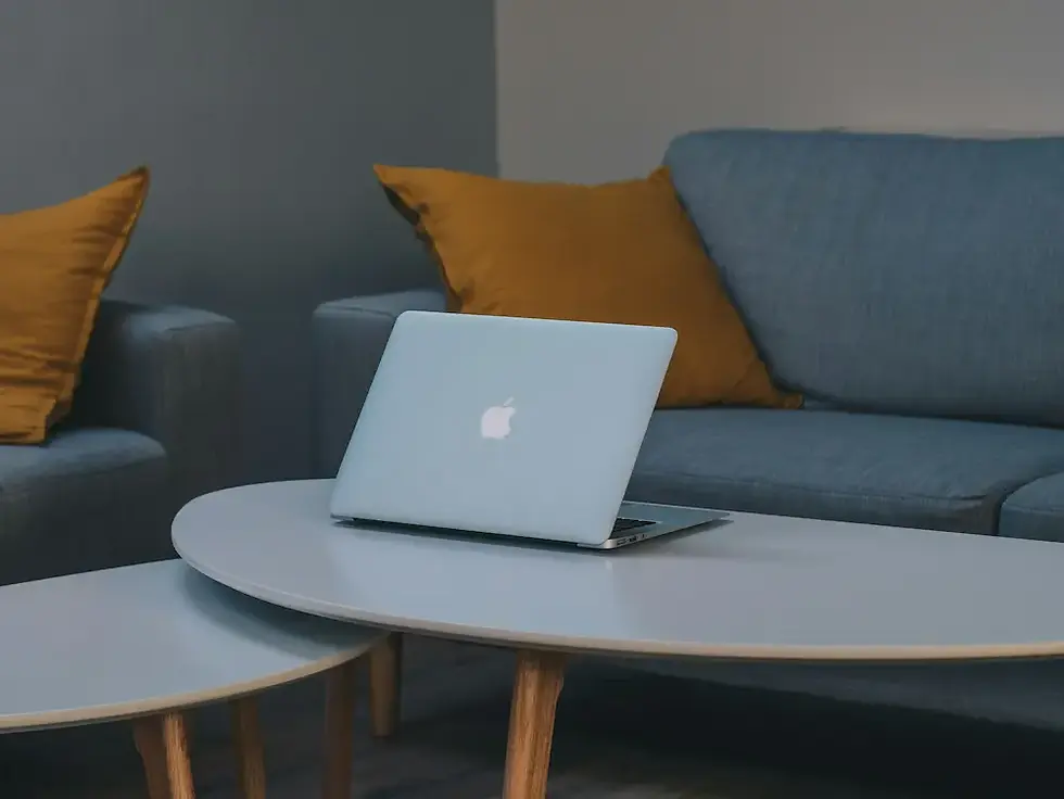 Two round nesting tables holding a laptop in front of a blue sofa with mustard cushions