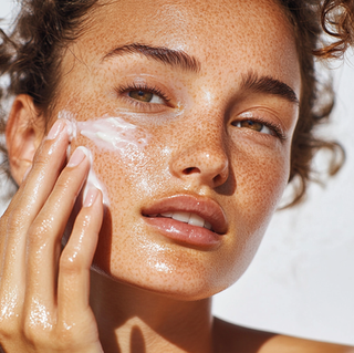 A woman in her 20's applying sun screen on her face
