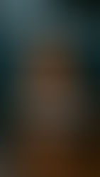 Professional woman in black blazer and glasses seated at a conference table in a glass-walled boardroom with a sports stadium in the background.