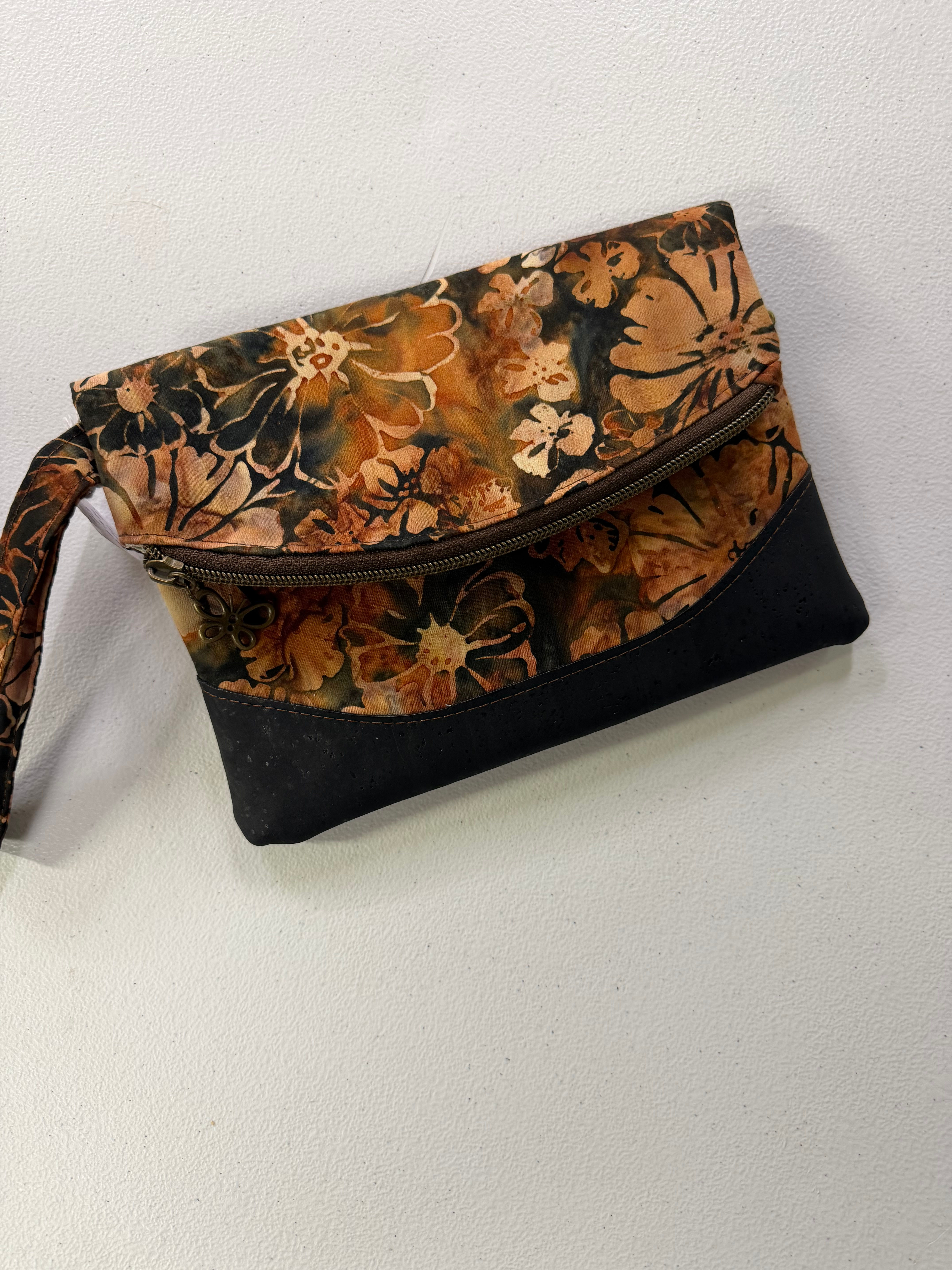 Front of clutch with curved zippere closure in brown floral batik and black cork trim