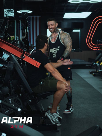 Trainer smiling while assisting a man on a gym machine at Alpha Gym | Alpha Gym Fitness | Orlando, Fl