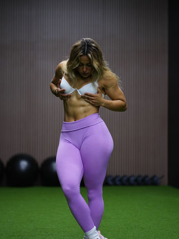Muscular woman in white sports bra and purple leggings. | Alpha Gym Fitness | Orlando, Fl