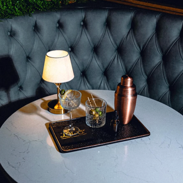 Cocktail shaker and drinks on a table with a small lamp.
