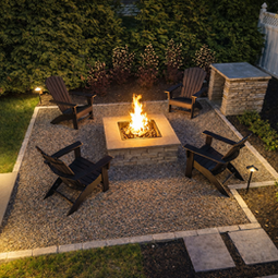 Backyard fire pit with burning fire, four Adirondack chairs, gravel patio. Custom fire pit | Down To Earth Landscaping | Jackson New Jersey, USA (732) 833-7702.