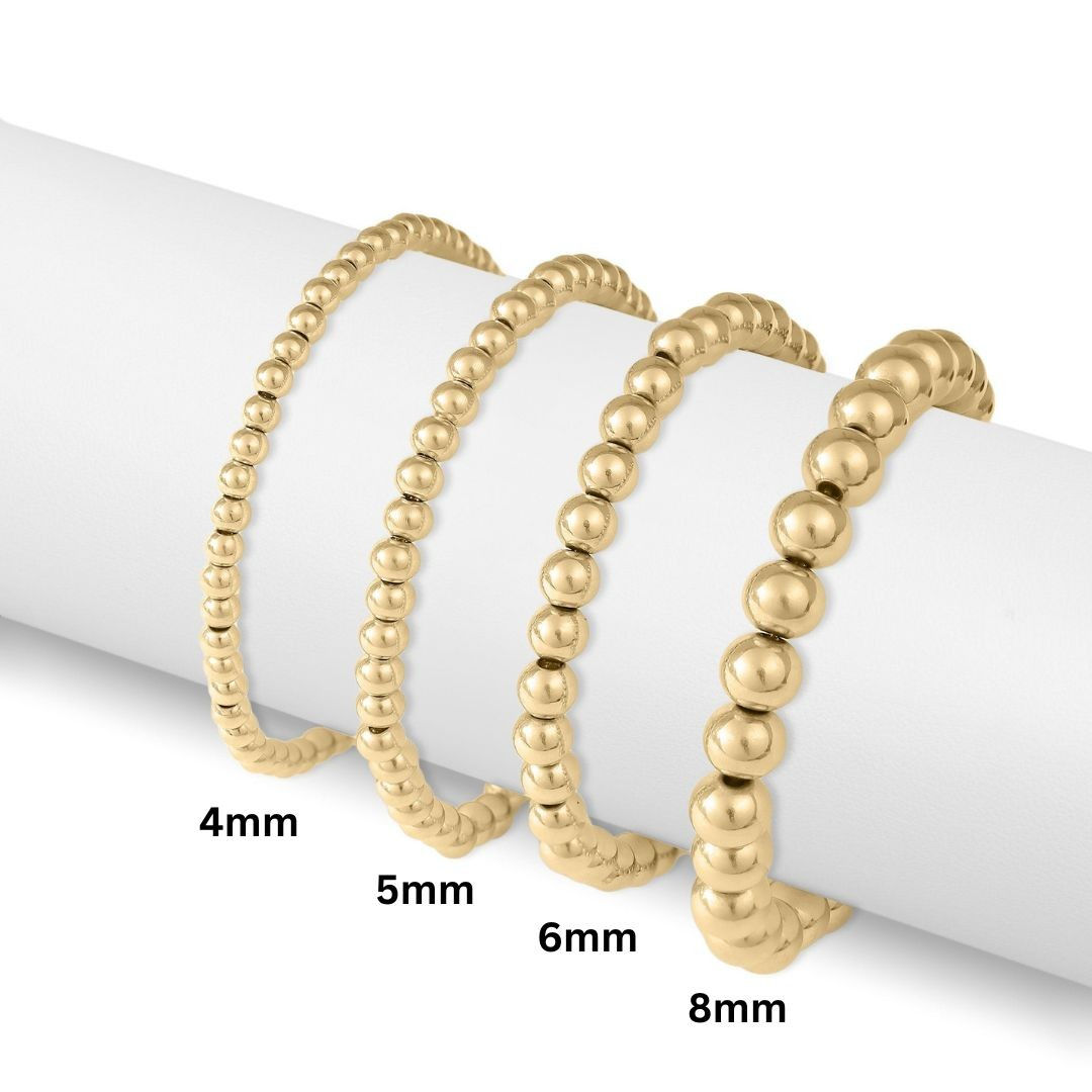 Stacked gold beaded stretch bracelets in 4mm, 5mm, 6mm, and 8mm bead sizes.