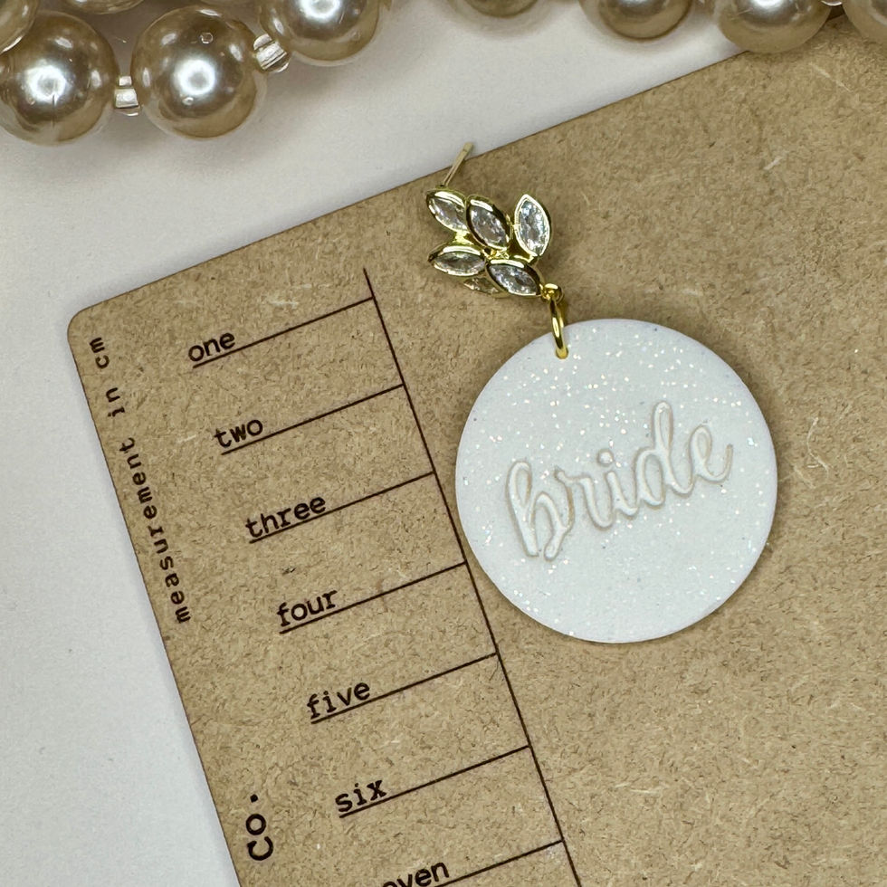 Bride earrings on a size reference card with ivory glitter clay disc, “bride” script, and gold CZ pavé accent.