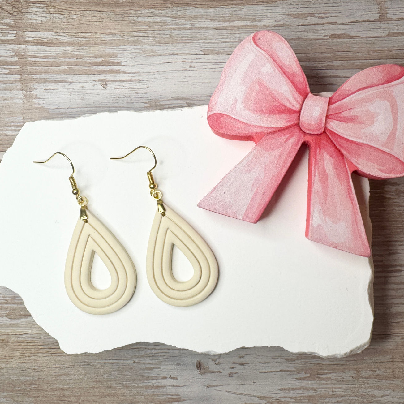 Elizabeth | Sculpted Polymer Clay Earrings (Cream) displayed on stone with pink bow.
