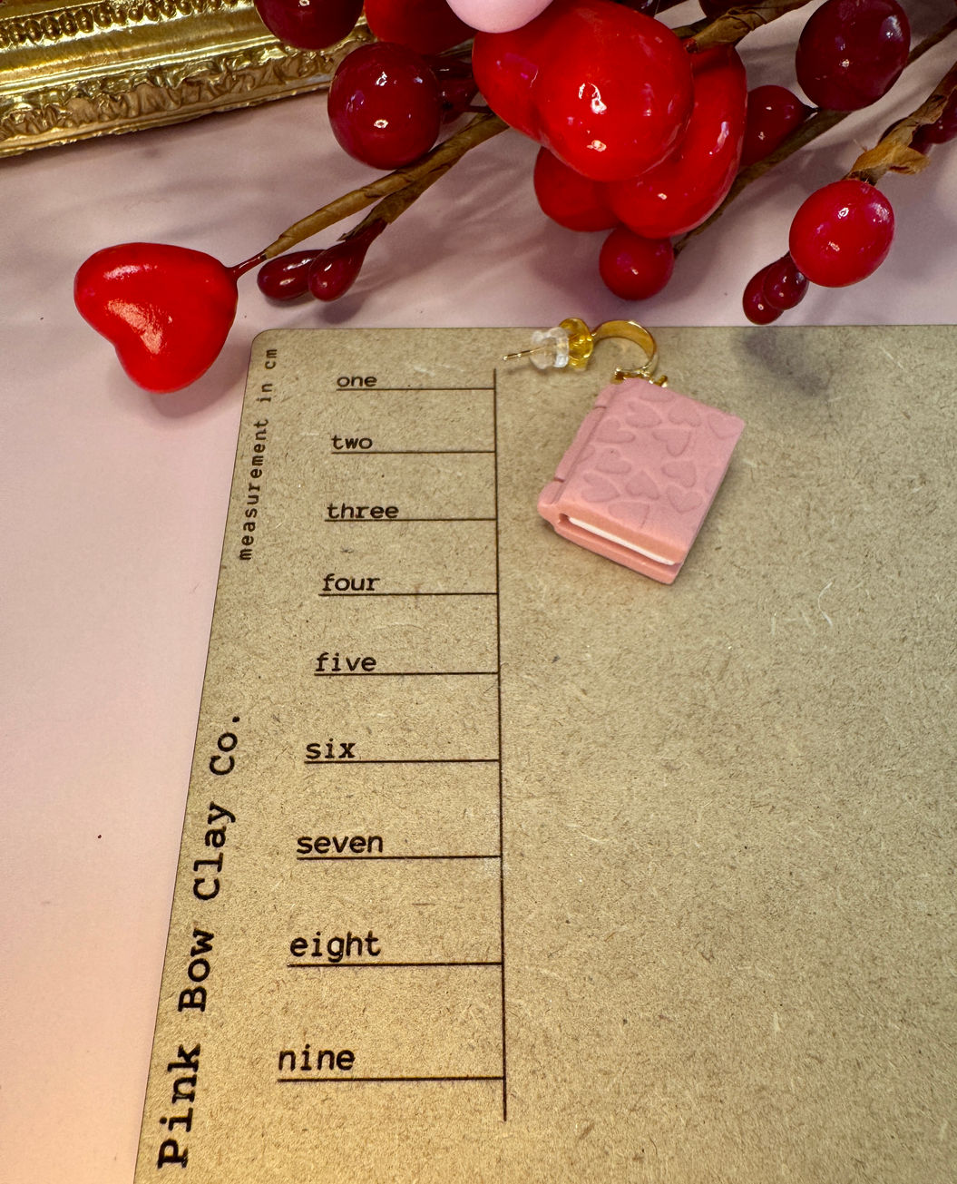 Small pink Book of Love earring on a measurement board
