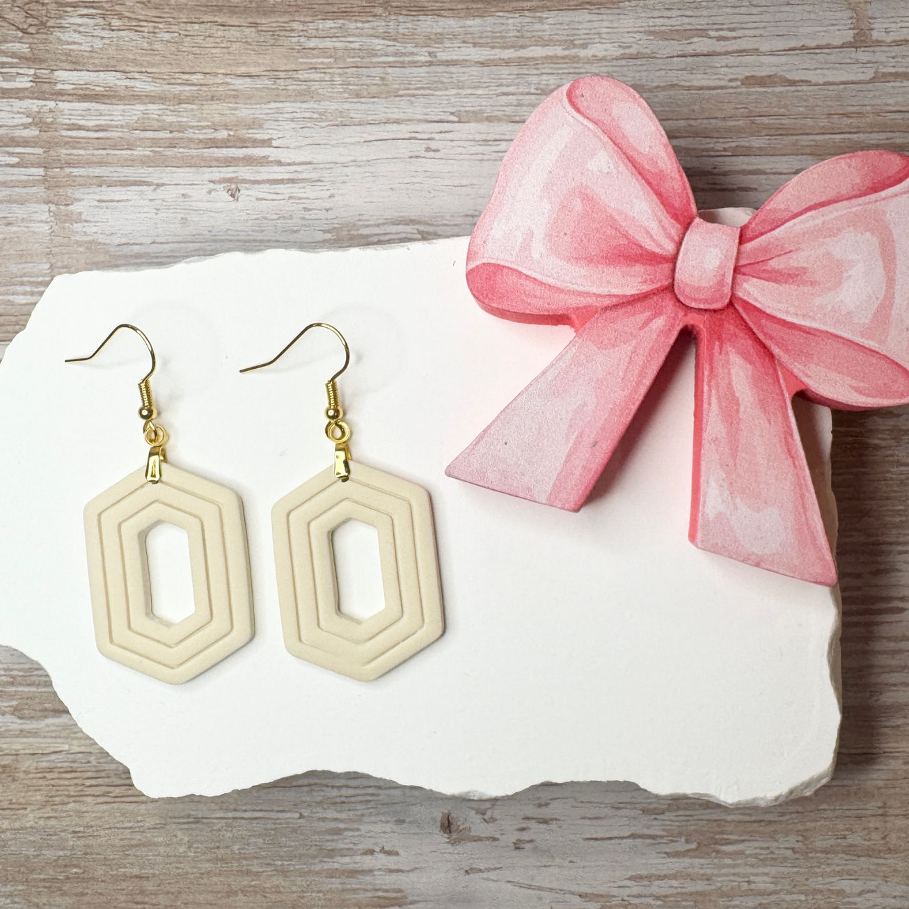 Cream Zelda geometric sculpted polymer clay earrings with gold-tone fishhook ear wires displayed with pink ribbon.