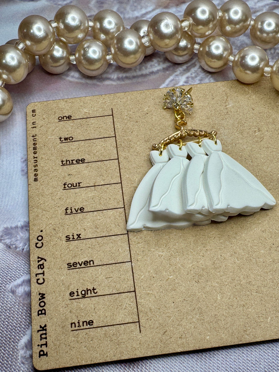 White polymer clay ballgown earring lying on a Pink Bow Clay Co. measurement board, showing layered skirt detail.