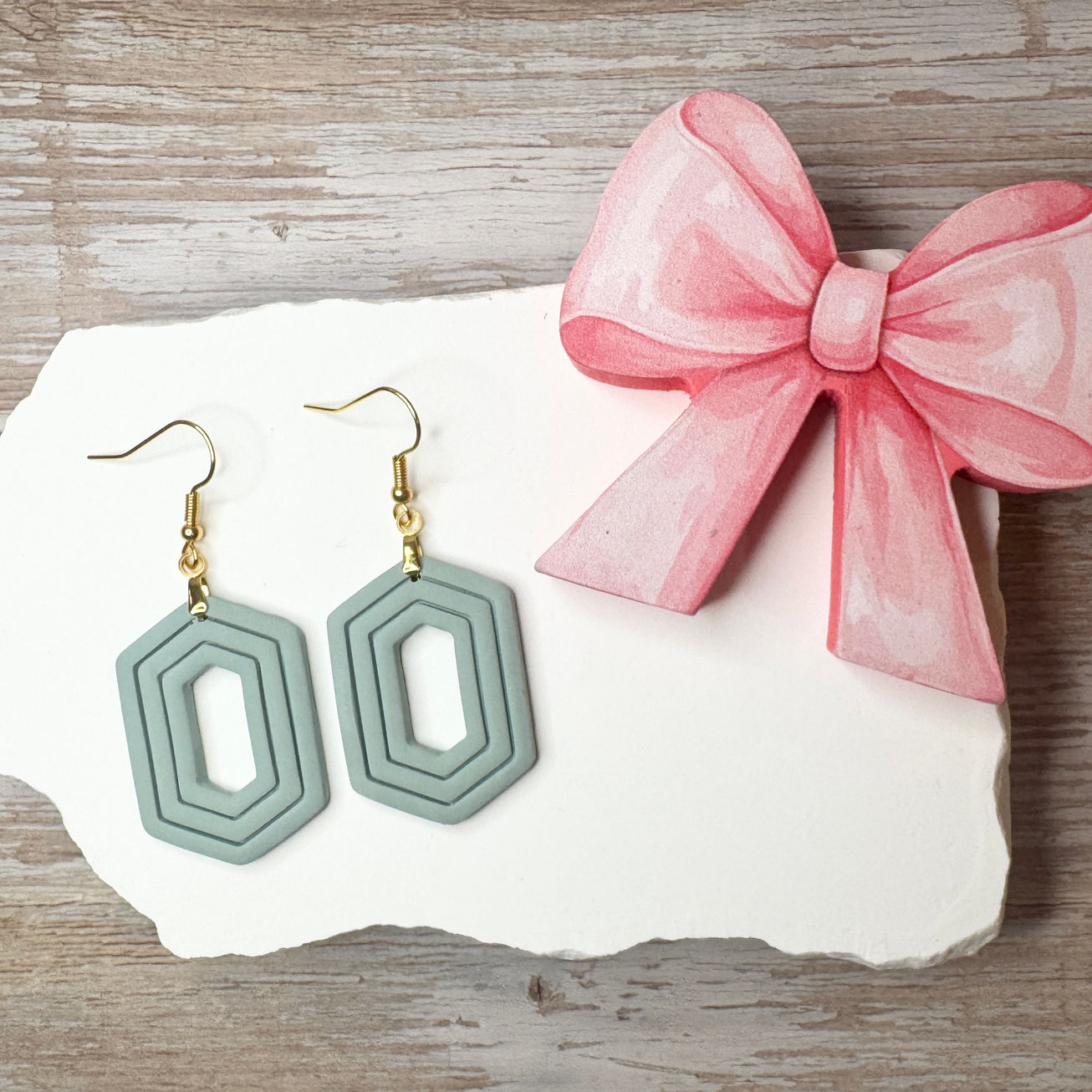 Seafoam Zelda geometric sculpted polymer clay earrings with gold-tone fishhook ear wires displayed with pink ribbon.
