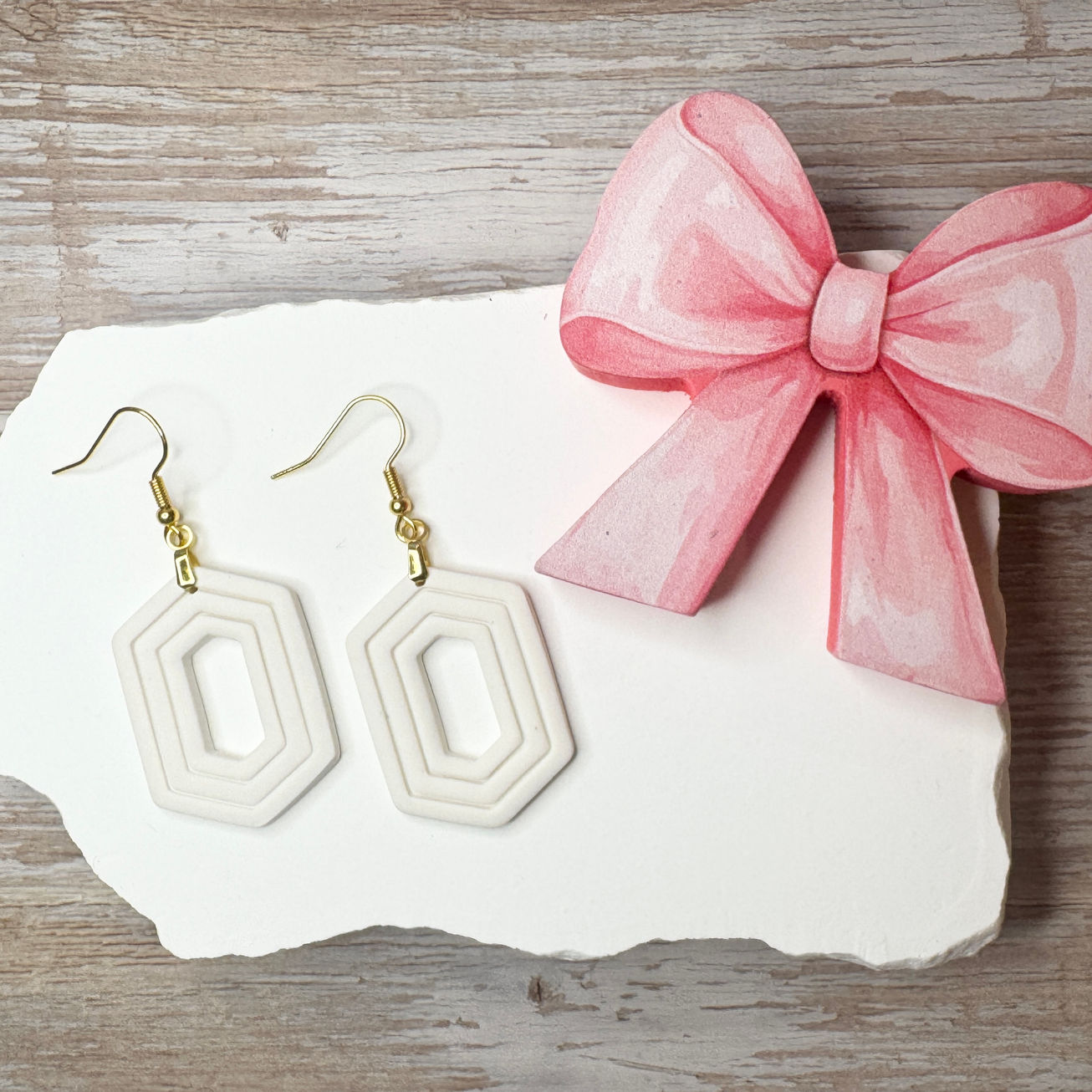 White Zelda geometric sculpted polymer clay earrings with gold-tone fishhook ear wires displayed with pink ribbon.