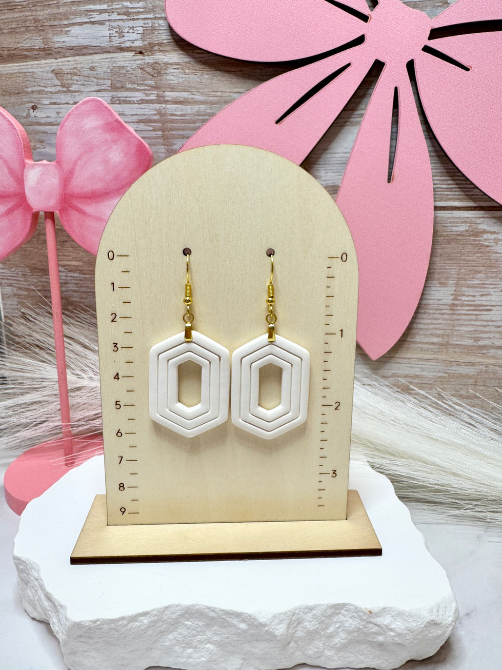 White Zelda geometric sculpted polymer clay earrings with gold-tone fishhook ear wires displayed on wooden jewelry stand.