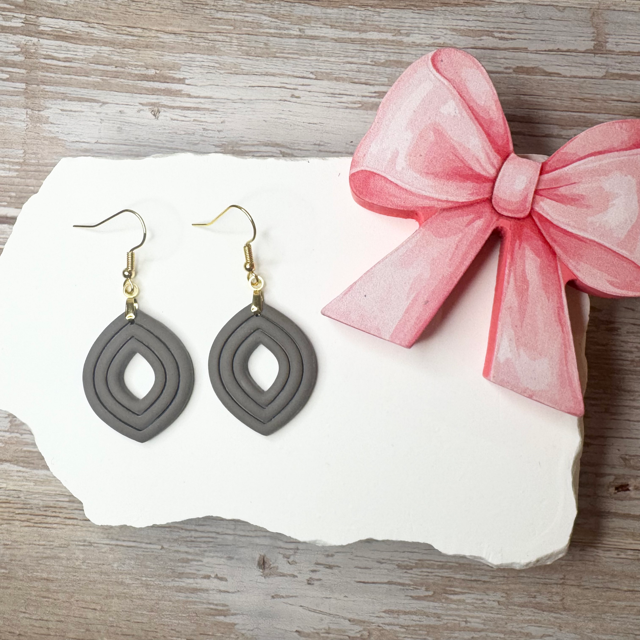 Clara | Sculpted Leaf Polymer Clay Earrings (Stone) displayed on white stone with a pink bow