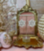 Metallic snowflake earrings on a stand in a gold frame