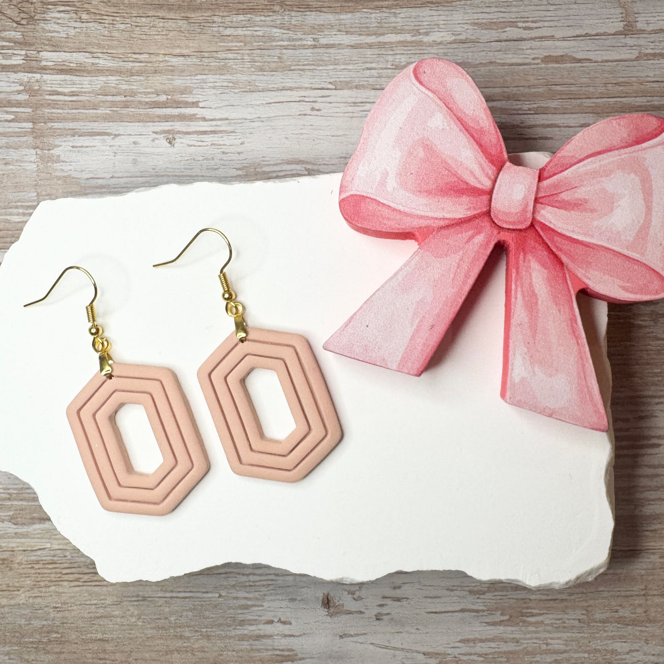 Fawn Zelda geometric sculpted polymer clay earrings with gold-tone fishhook ear wires displayed with pink ribbon.
