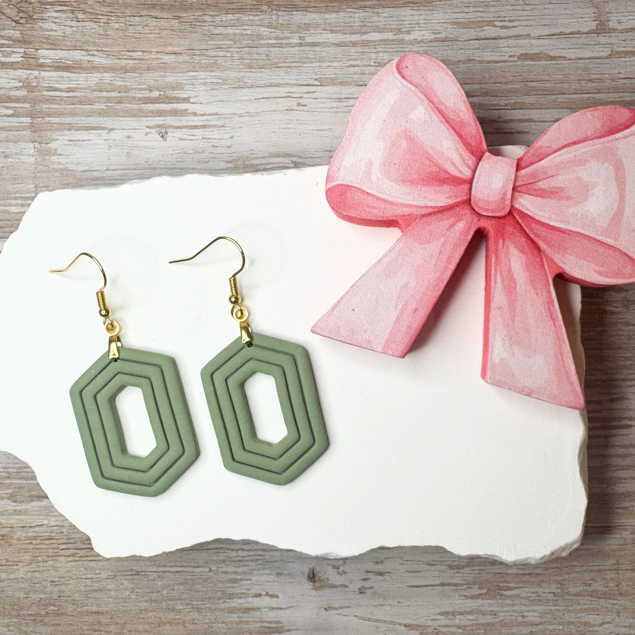 Moss Zelda geometric sculpted polymer clay earrings with gold-tone fishhook ear wires displayed with pink ribbon.