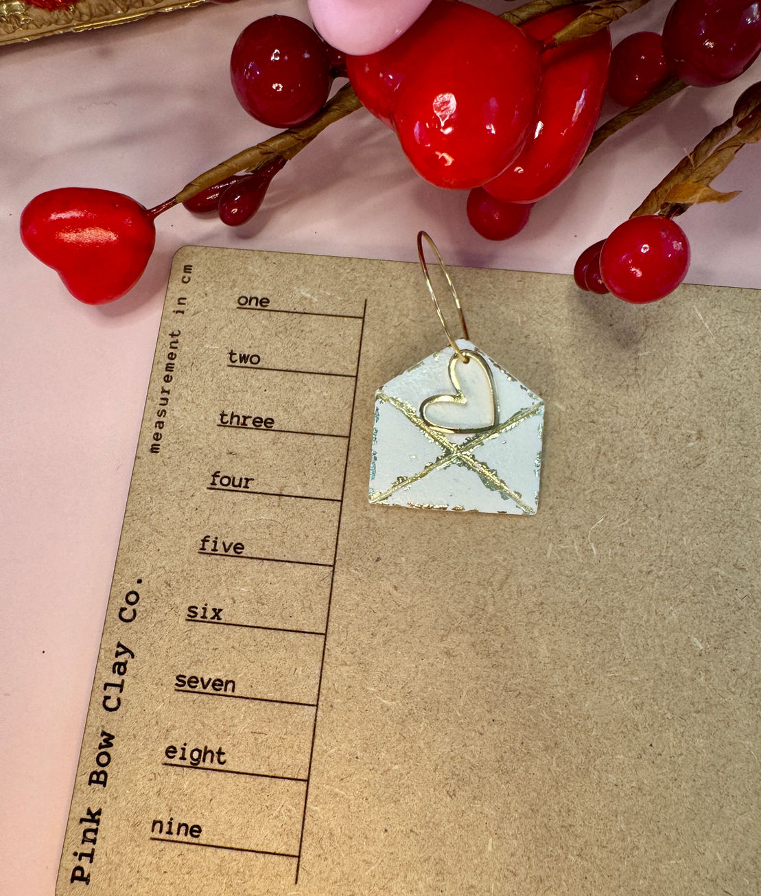 Golden love letter envelope earring on a measuring card.