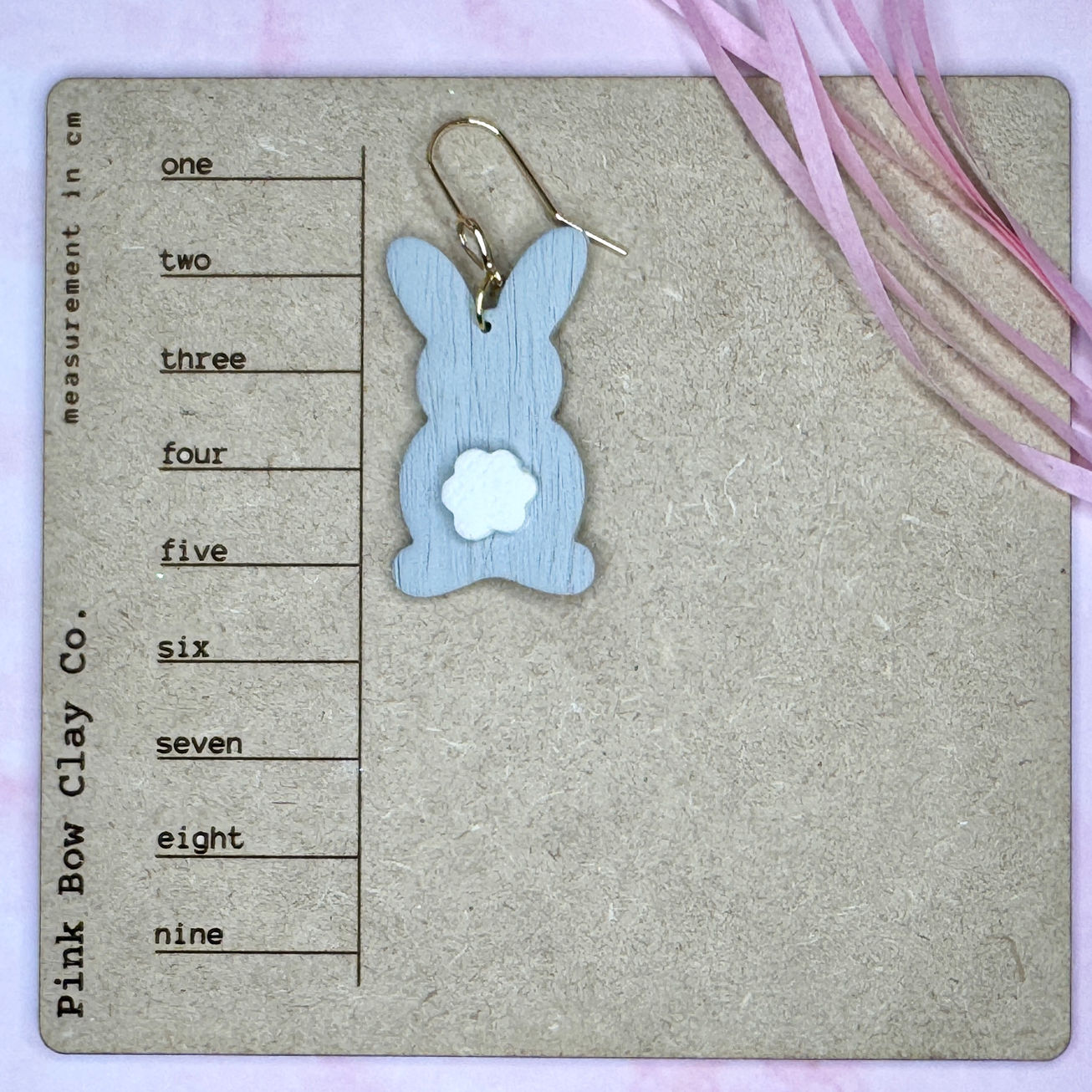 Gray polymer clay bunny earrings with white cotton tails and gold CZ pavé hooks displayed on ruler card.