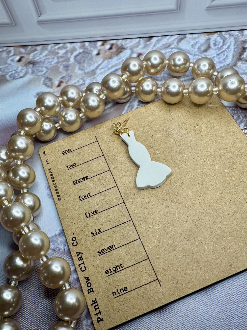 Single white bridal gown–shaped clay earring on a measurement card with gold floral CZ stud.