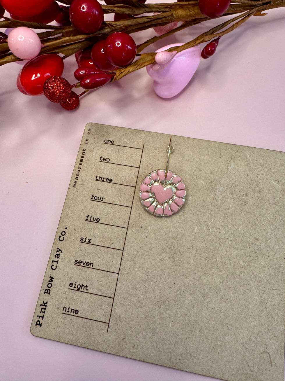 Round coin shaped earring with an embossed gold foil heart on measurement board.
