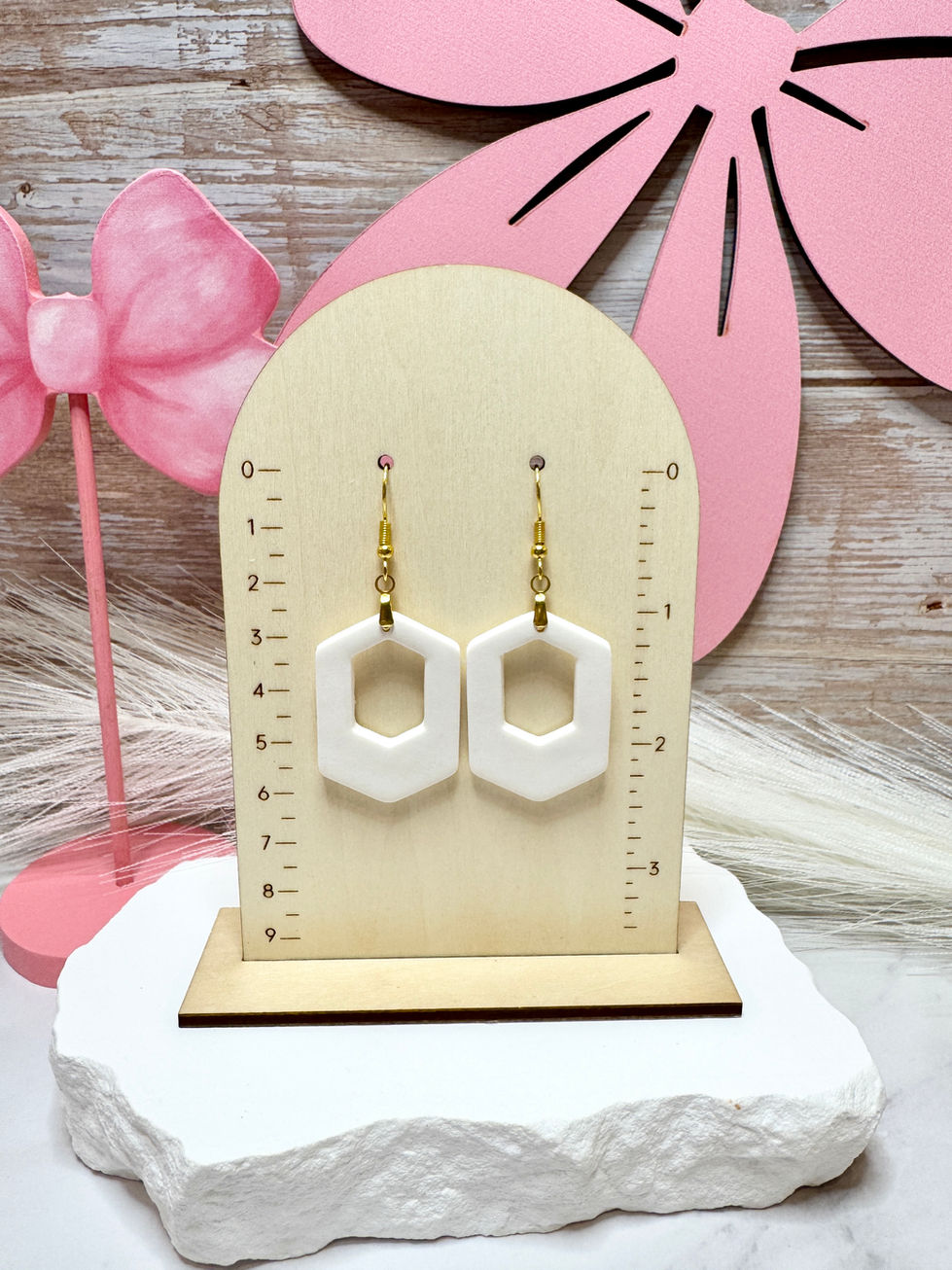 White Zelda-Offset Geometric Polymer Clay Earrings displayed on a wooden jewelry stand with pink bow accents