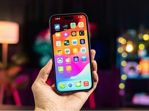 Main tenant un iPhone récent avec écran OLED allumé, en intérieur, éclairage chaleureux — illustration du service de réparation écran iPhone OLED à Saint-Tropez (LANDPC).