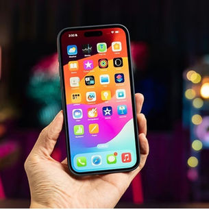 Main tenant un iPhone récent avec écran OLED allumé, en intérieur, éclairage chaleureux — illustration du service de réparation écran iPhone OLED à Saint-Tropez (LANDPC).
