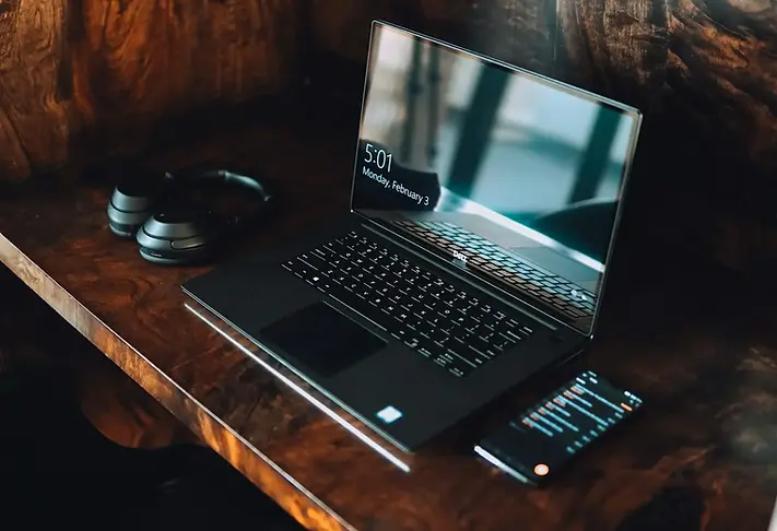 Ordinateur portable Dell noir sur bureau en bois, casque audio à côté, service de réparation PC à distance en France