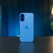 iPhone 16 bleu posé verticalement sur une table, avec un éclairage d’ambiance flou en arrière-plan dans un intérieur moderne