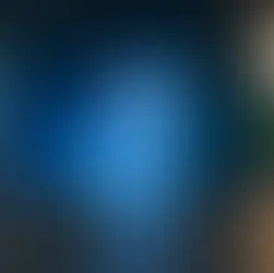 iPhone 16 bleu posé verticalement sur une table, avec un éclairage d’ambiance flou en arrière-plan dans un intérieur moderne