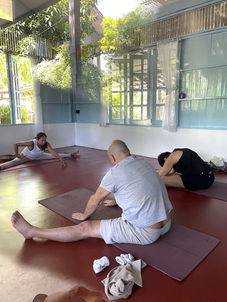 two men doing yoga, guided by a female yoga teacher inside a room