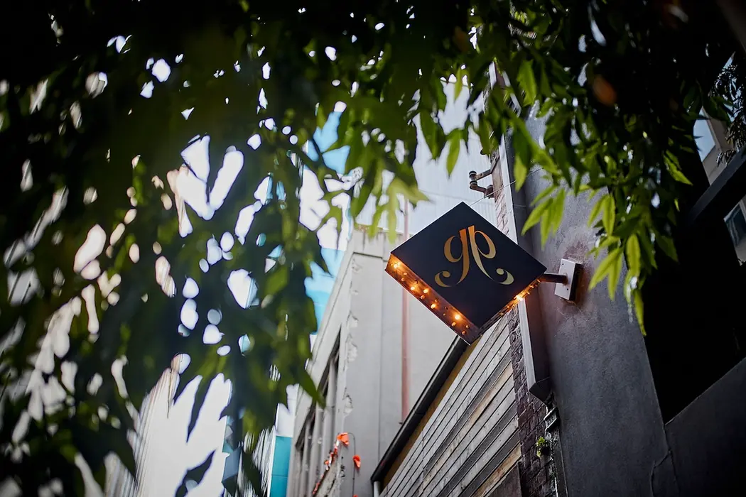 Exterior view of the Gin Palace bar, with an illuminated sign framed by foliage. 