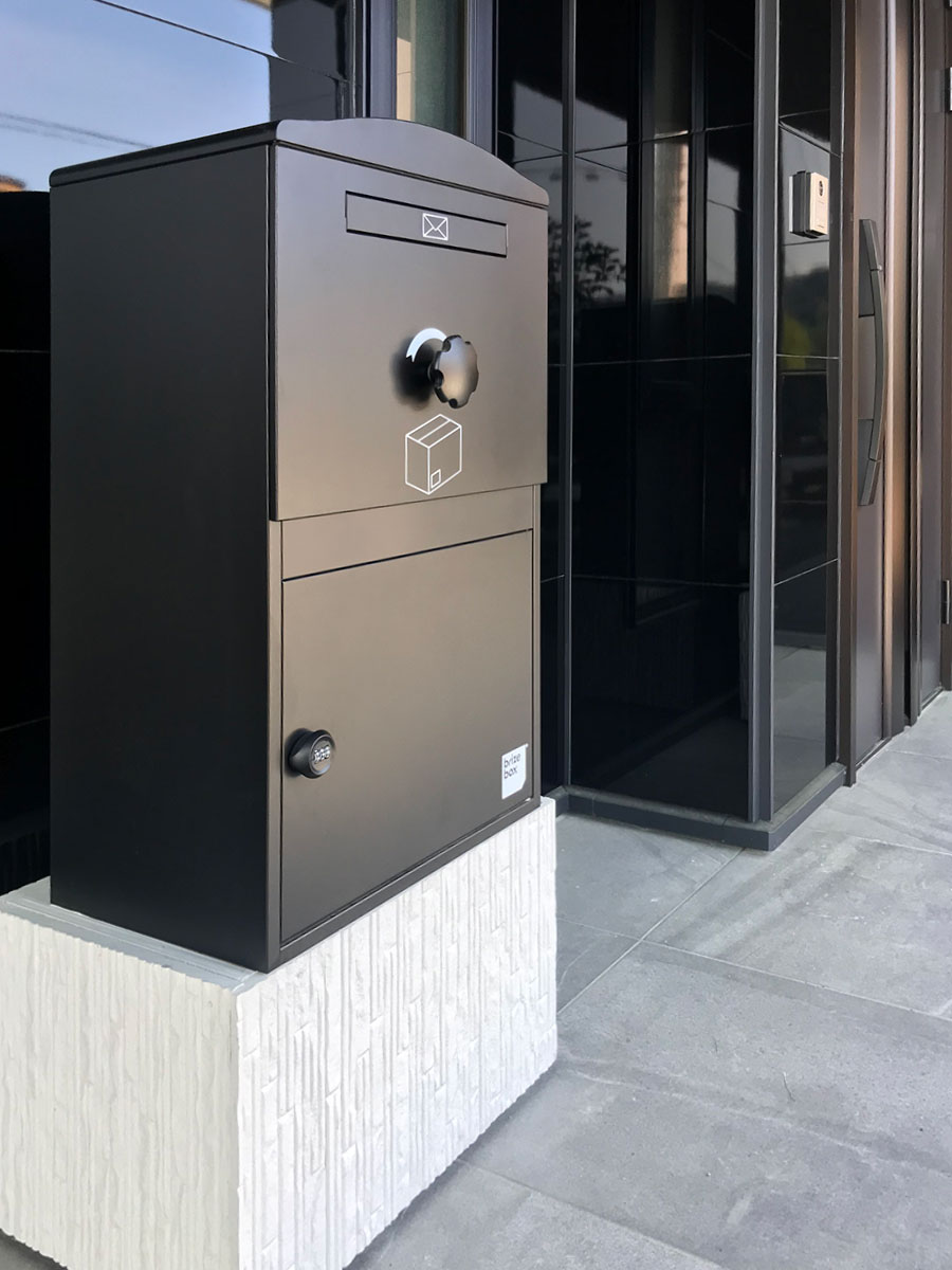 戸建て玄関前に設置されたブラックの大容量宅配ボックス。シンプルで高級感ある外観に調和し、不在時でも安心して荷物を受け取れます。