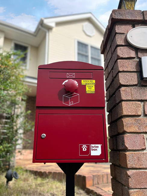 戸建て玄関前に設置された赤い宅配ボックス。レンガ調の門柱や外観と調和し、不在時でも安心して荷物を受け取れる便利な宅配ボックスです。