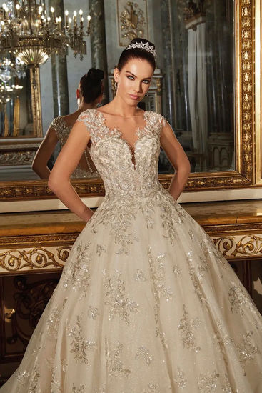 Glisten in the elegance of the ORIANA gown. This ball gown features glimmering beaded lace atop sparkling tulle with it’s sophisticated Cap sleeves and deep sweetheart neckline. These shimmering details continue to the back of the design with a sexy button up illusion back.