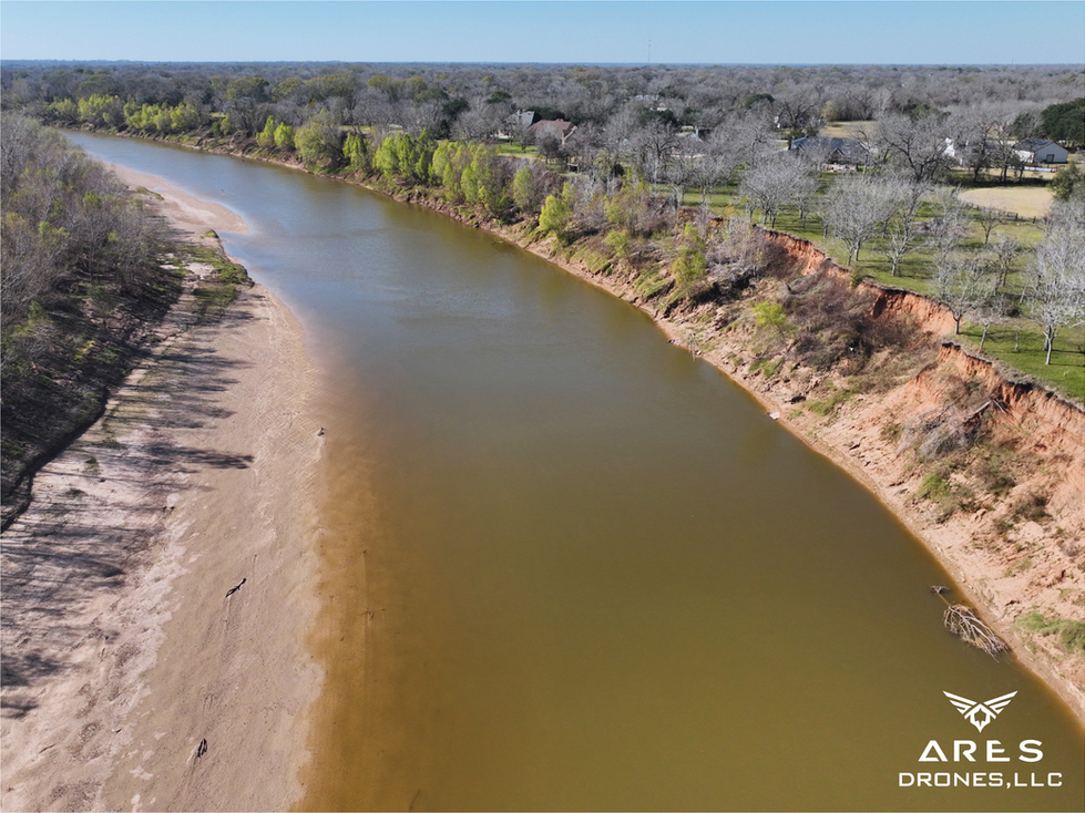 Aerial image of bank erosion and sandbar formation along the Brazos River in Rosenberg, Texas, documenting channel migration and floodplain features.