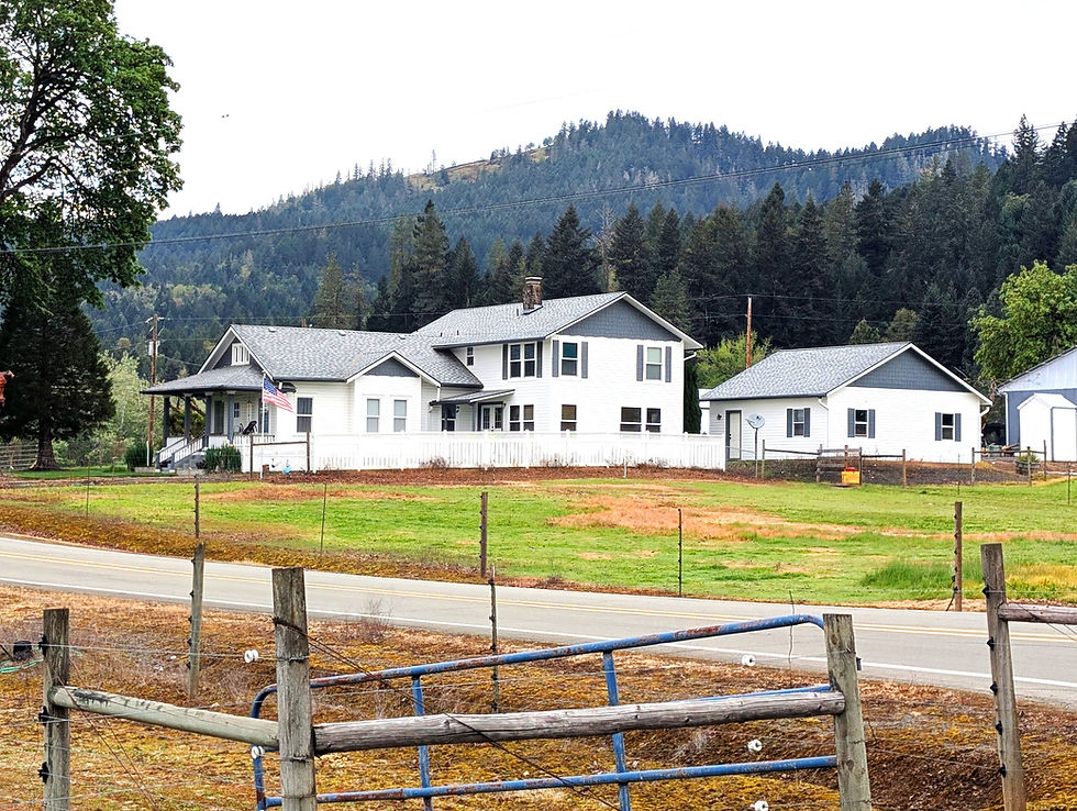 White house with porch, outbuilding, and wooded mountains