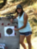 A lady standing at an archery target with an arrow in the bullseye at archery camp.